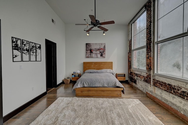 bedroom featuring visible vents, ceiling fan, brick wall, wood finished floors, and baseboards