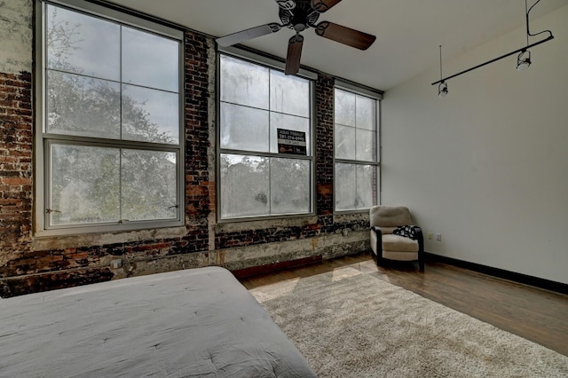 unfurnished bedroom featuring brick wall, baseboards, ceiling fan, and wood finished floors