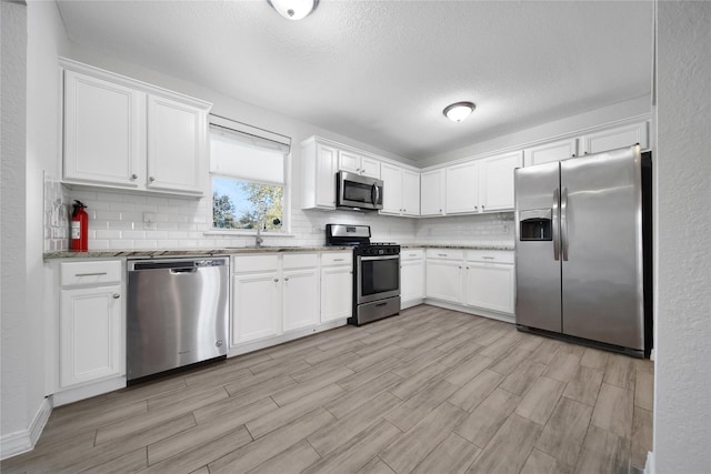 kitchen featuring light stone counters, appliances with stainless steel finishes, backsplash, and white cabinetry