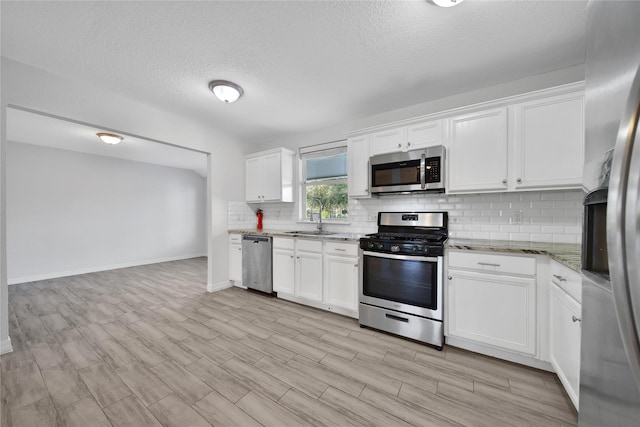 kitchen featuring light stone counters, decorative backsplash, appliances with stainless steel finishes, white cabinetry, and a sink