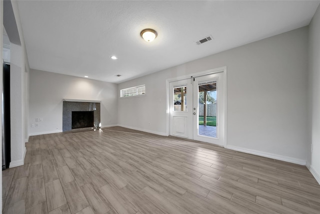 unfurnished living room featuring baseboards, a premium fireplace, visible vents, and wood finished floors