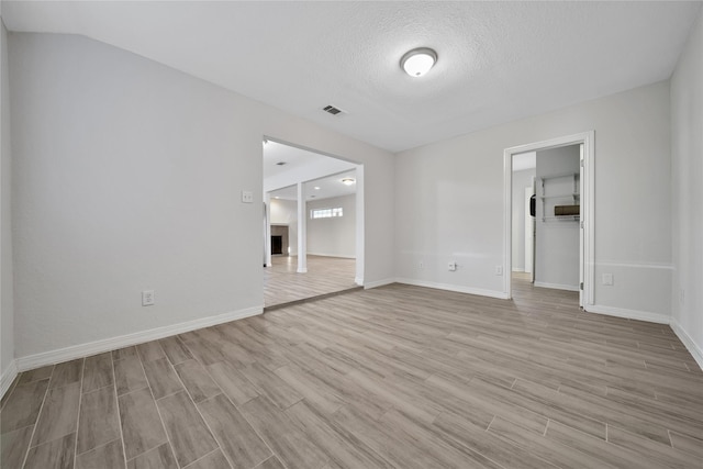 empty room featuring light wood-style floors, a fireplace, baseboards, and a textured ceiling