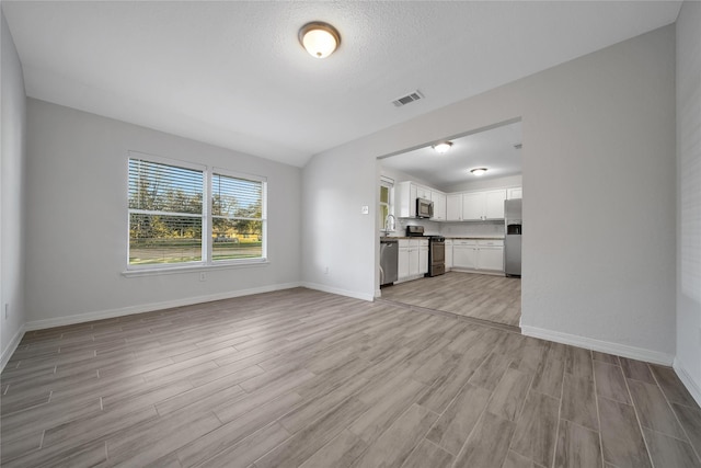 unfurnished living room featuring a textured ceiling, a sink, visible vents, baseboards, and light wood-style floors