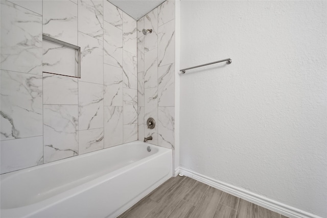 bathroom with a textured wall, wood finish floors, washtub / shower combination, and baseboards