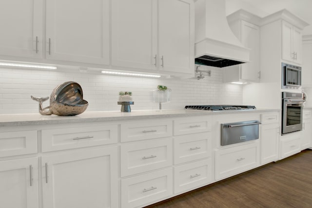 kitchen featuring dark wood-style floors, a warming drawer, stainless steel appliances, white cabinets, and premium range hood