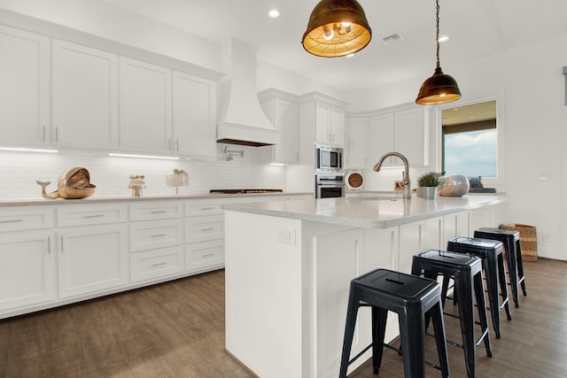 kitchen featuring custom range hood, appliances with stainless steel finishes, white cabinetry, a sink, and wood finished floors