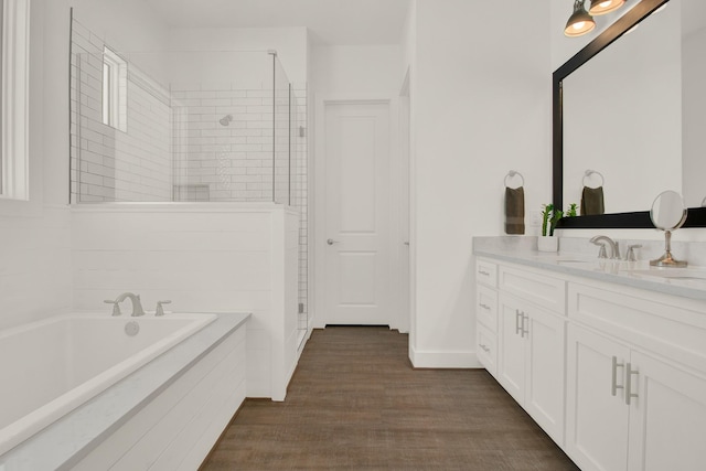 bathroom with wood finished floors, vanity, baseboards, tiled shower, and a bath