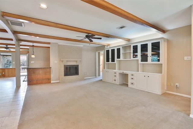 unfurnished living room with ceiling fan, beamed ceiling, a brick fireplace, and built in study area