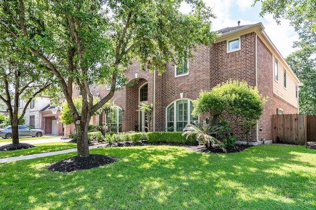 view of front facade with brick siding, a front yard, and fence