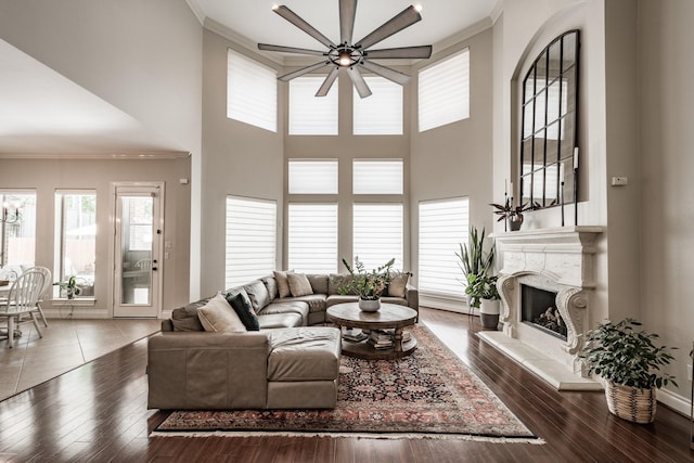 living area featuring baseboards, a ceiling fan, wood finished floors, crown molding, and a fireplace