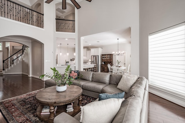 living area featuring arched walkways, dark wood-style flooring, stairs, and a towering ceiling