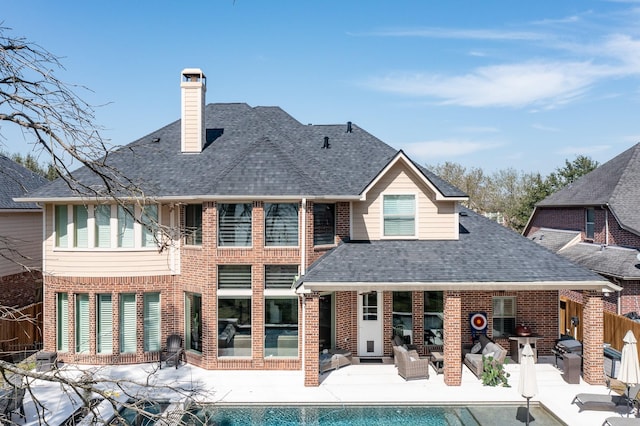 rear view of house with a patio area, brick siding, a chimney, and a shingled roof