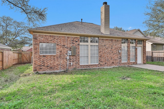 back of property with a shingled roof, a lawn, a fenced backyard, a chimney, and brick siding