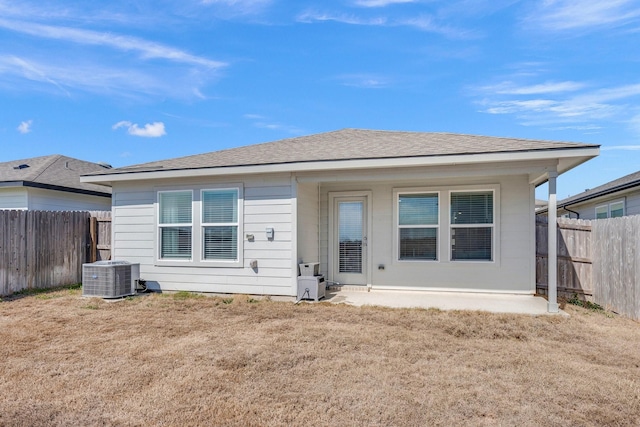 back of property with fence private yard, a shingled roof, central AC unit, and a yard