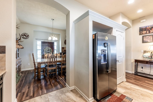 kitchen with arched walkways, wood finished floors, baseboards, stainless steel fridge with ice dispenser, and an inviting chandelier