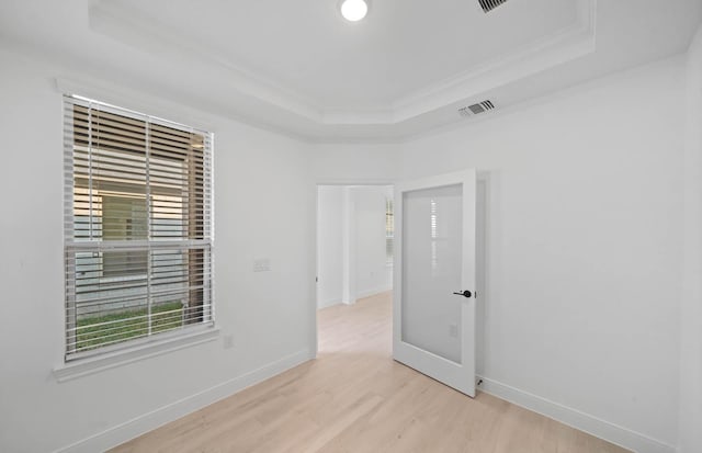 unfurnished room featuring a tray ceiling, visible vents, ornamental molding, light wood-style floors, and baseboards