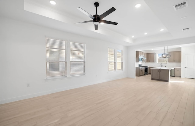 unfurnished living room with light wood-style flooring, visible vents, a raised ceiling, and baseboards