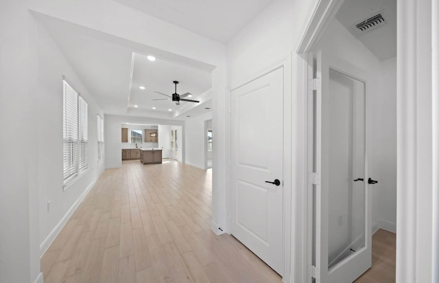 hallway with recessed lighting, visible vents, baseboards, light wood finished floors, and a tray ceiling