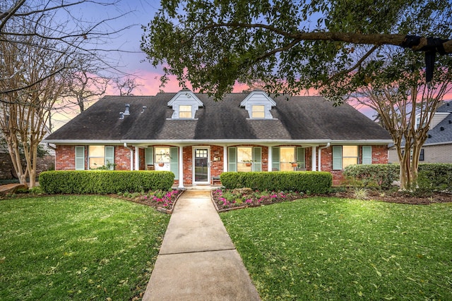 cape cod home featuring a yard, brick siding, and a shingled roof