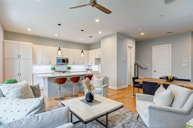 living area featuring recessed lighting, visible vents, light wood-style flooring, baseboards, and stairs