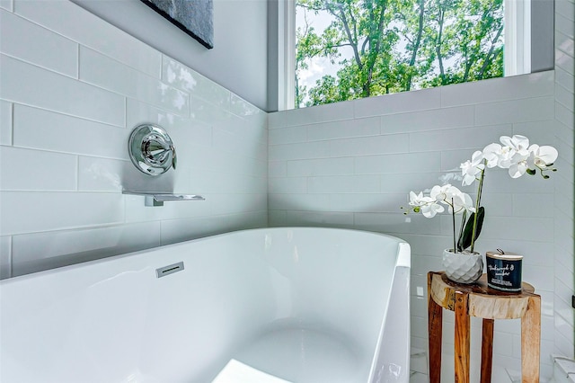 full bath featuring a freestanding tub, a healthy amount of sunlight, and tile walls