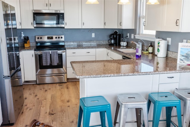 kitchen featuring light wood-style flooring, appliances with stainless steel finishes, white cabinets, light stone countertops, and a peninsula