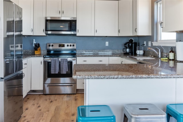 kitchen with appliances with stainless steel finishes, a sink, a peninsula, and dark stone countertops