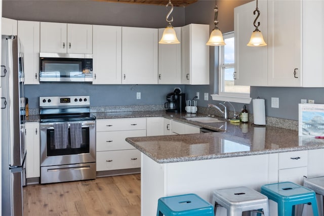 kitchen with light wood-style flooring, a peninsula, stainless steel appliances, white cabinetry, and a sink