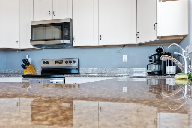 kitchen featuring stainless steel appliances, stone counters, white cabinets, and a sink