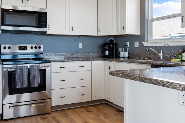 kitchen with appliances with stainless steel finishes, white cabinets, a sink, and wood finished floors