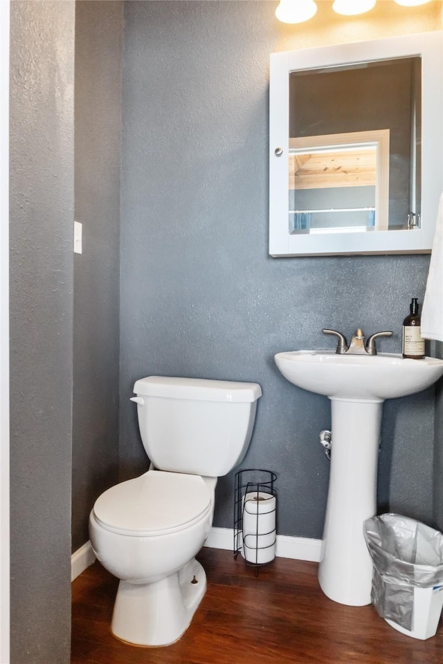 half bath featuring toilet, baseboards, wood finished floors, and a textured wall