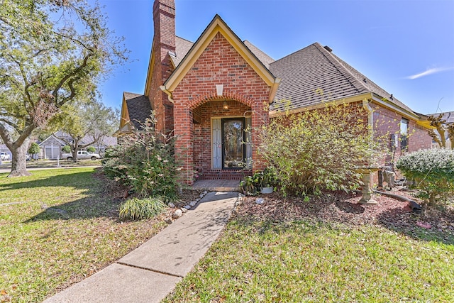 view of front facade with a front yard, brick siding, a chimney, and roof with shingles