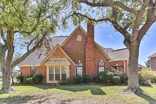 tudor house featuring a shingled roof, a front yard, brick siding, and a chimney