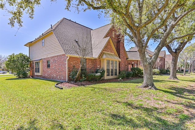 view of front of property featuring roof with shingles, a front yard, a chimney, and brick siding