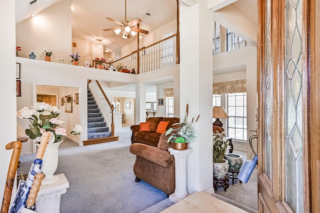 living room with visible vents, stairway, a towering ceiling, a ceiling fan, and carpet flooring