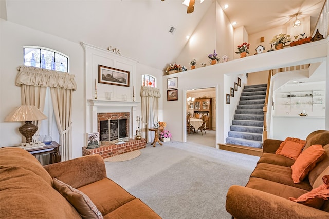 carpeted living area with high vaulted ceiling, a brick fireplace, visible vents, and stairway