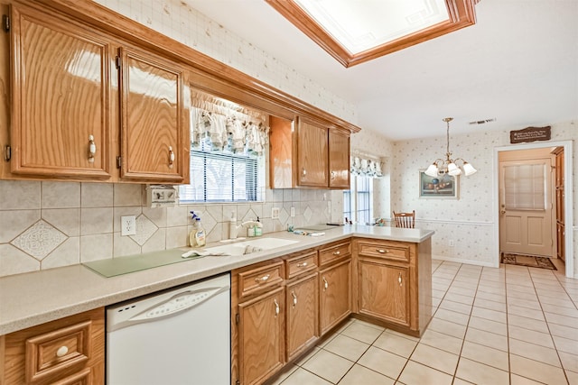 kitchen with white dishwasher, a peninsula, a healthy amount of sunlight, light countertops, and wallpapered walls