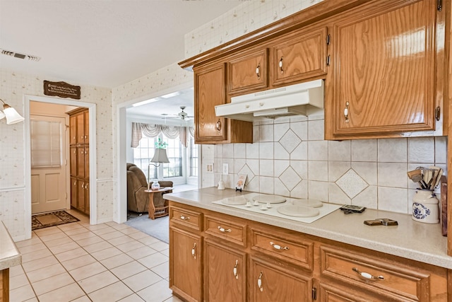 kitchen with wallpapered walls, white electric stovetop, brown cabinetry, light countertops, and under cabinet range hood