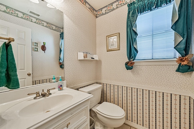 bathroom with a wainscoted wall, vanity, toilet, and wallpapered walls