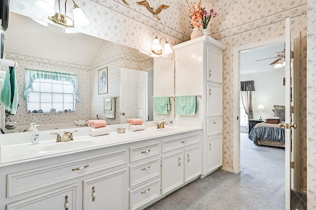 ensuite bathroom featuring double vanity, wallpapered walls, a ceiling fan, connected bathroom, and a sink