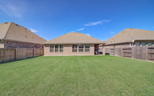 back of property featuring a fenced backyard, a yard, brick siding, and roof with shingles