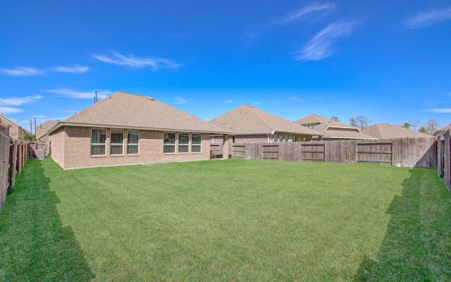 rear view of property with brick siding, a fenced backyard, and a yard