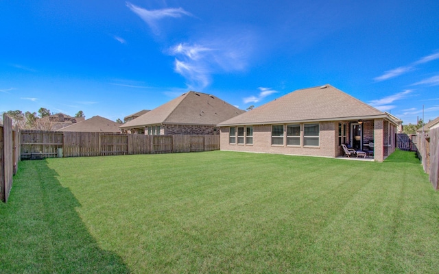 back of house with a fenced backyard, brick siding, roof with shingles, a lawn, and a patio area