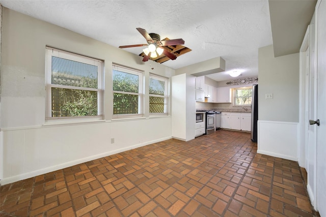 kitchen with brick floor, a ceiling fan, baseboards, white cabinets, and appliances with stainless steel finishes