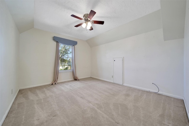 carpeted empty room featuring a textured ceiling, ceiling fan, vaulted ceiling, and baseboards