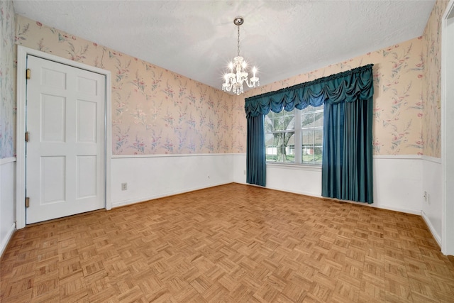 empty room with a textured ceiling, wainscoting, a chandelier, and wallpapered walls