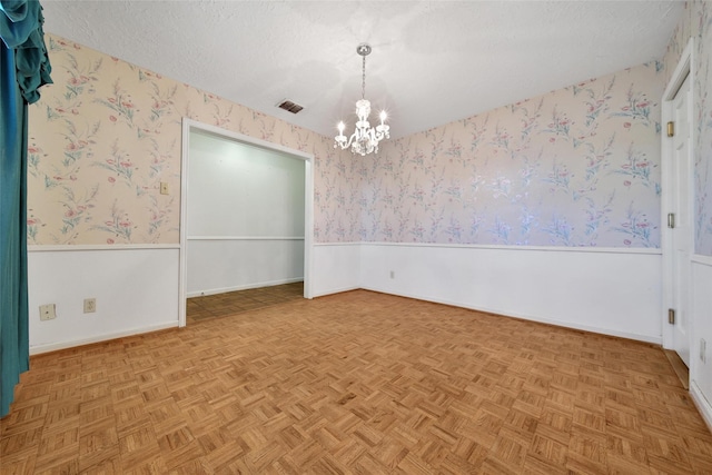 empty room with a textured ceiling, a chandelier, a wainscoted wall, visible vents, and wallpapered walls