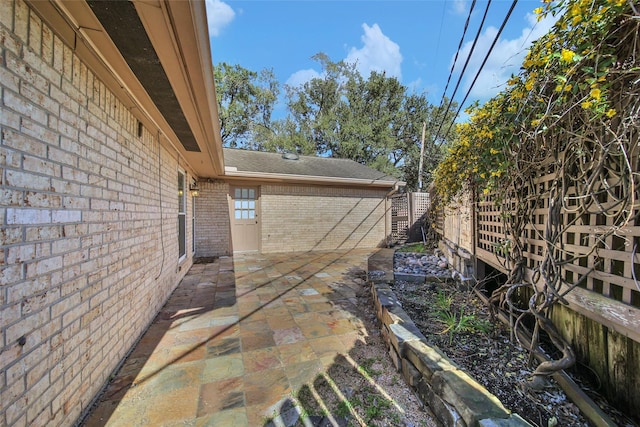 view of property exterior featuring a shingled roof, a patio area, brick siding, and fence