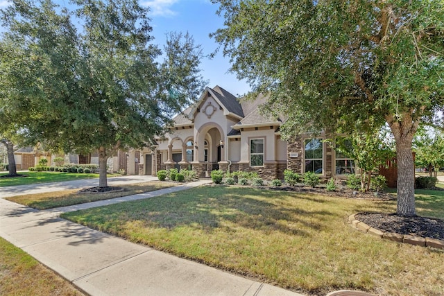 view of front of home featuring stone siding, concrete driveway, a front lawn, and stucco siding