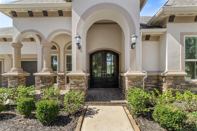 view of exterior entry with stone siding, roof with shingles, french doors, and stucco siding